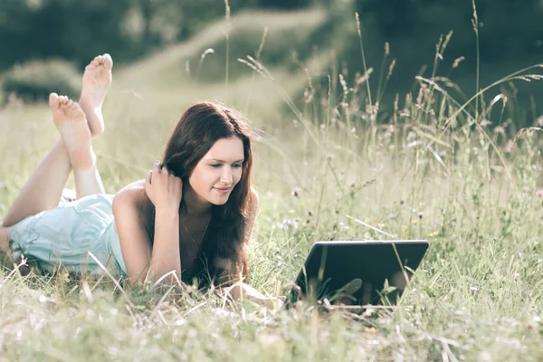 Söt flicka tittar på skärmen på sin bärbara dator när du ligger på gräset — Stockfoto