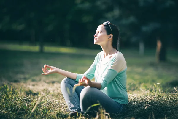 美しい若い女性が芝生の上に座ってロータスの位置で瞑想. — ストック写真
