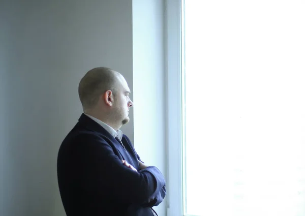 Homem de negócios pensativo olhando para uma janela de escritório em branco — Fotografia de Stock