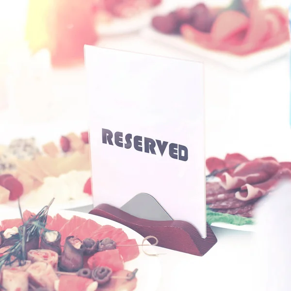A reserved sign on the restaurant table in bright sunny weather against a background of dishes — Stock Photo, Image