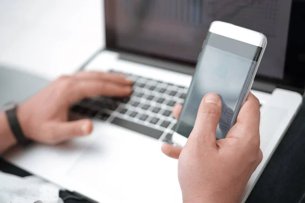 Close up. the businessman uses a smartphone and a laptop in the workplace. — 图库照片