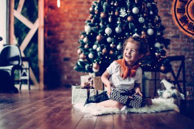 Meraklı küçük kız Noel ağacının yanında oturuyor .