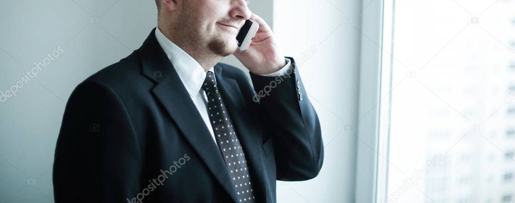 handsome pensive businessman using smartphoone and looking through window in the office.