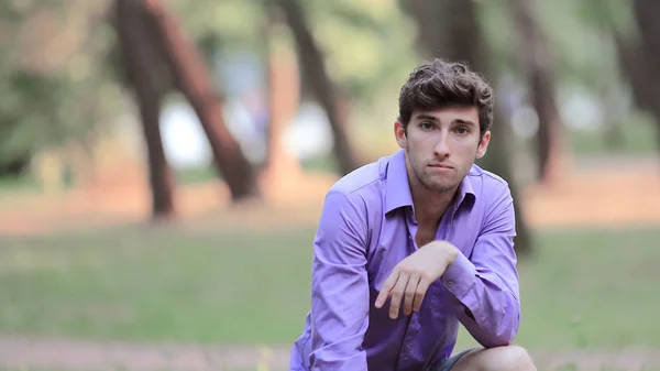 Guy in casual clothes sits on lawn in park — Stock Photo, Image