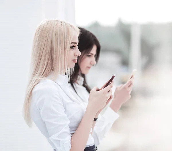 Unge kvinnelige ansatte i foretaket utveksler informasjon om en smarttelefon – stockfoto