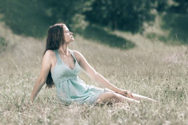 Güzel genç bir kadın yaz günü ormanlık alanda oturuyor.