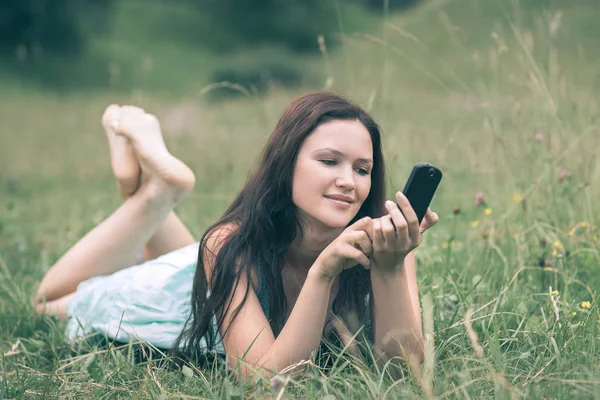 Attraktive junge Frau benutzt ihr Smartphone, während sie auf einer Lichtung liegt — Stockfoto