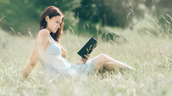 Chica estudiante leyendo un libro sentado en el césped en un día de verano —  Fotos de Stock
