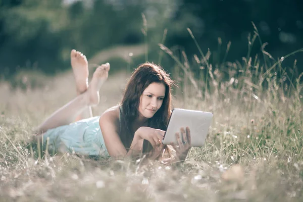 Söt flicka med digital tablett liggande på gräsmattan på sommardag — Stockfoto