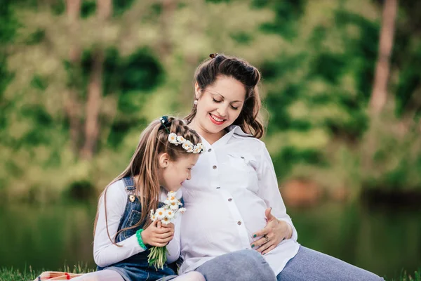 Bella donna incinta con la sua piccola figlia seduta sul prato — Foto Stock