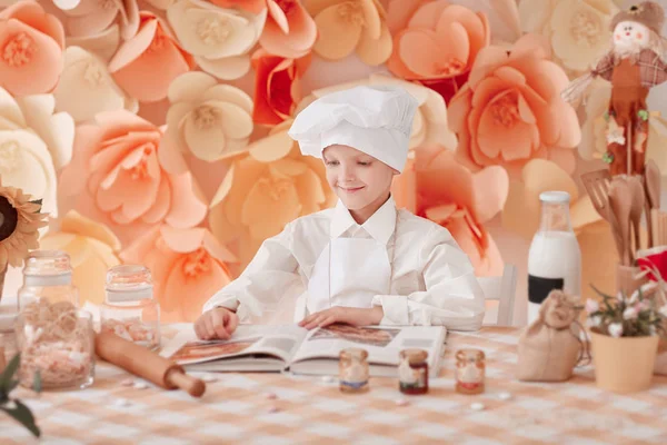 Niño feliz en un uniforme de chefs está leyendo un libro de cocina —  Fotos de Stock