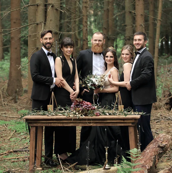 Ospiti e un paio di novelli sposi vicino al tavolo da picnic nel bosco — Foto Stock