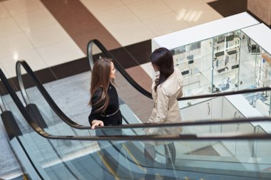 iki iş kadının bir iş merkezinde bir yürüyen merdiven üzerinde gülümseyen