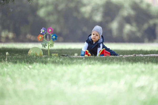 Mały chłopak siedzi na trawniku w dniu wiosny — Zdjęcie stockowe