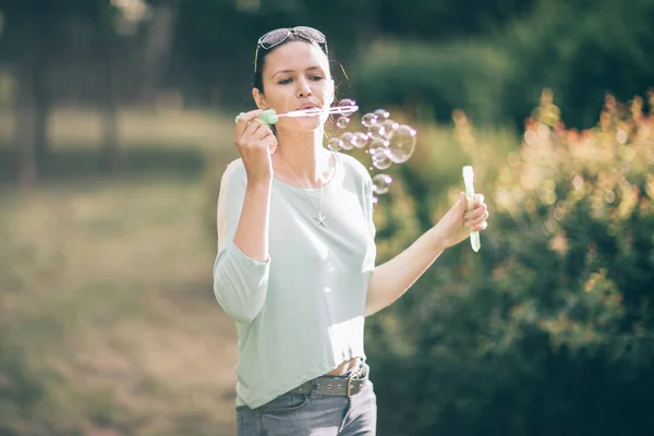 Attractive young woman blowing bubbles in summer Park — Stock Photo, Image