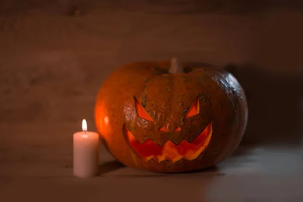 Vela y una calabaza de Halloween sonriente espeluznante en una mesa de madera —  Fotos de Stock