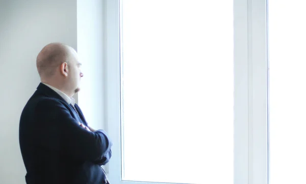 Homem de negócios pensativo olhando para uma janela de escritório em branco — Fotografia de Stock