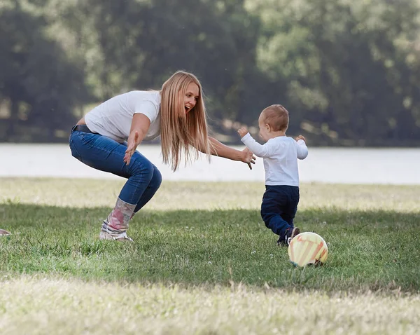 Mamma, papà e il loro piccolo figlio stanno giocando con la palla sul prato . — Foto Stock