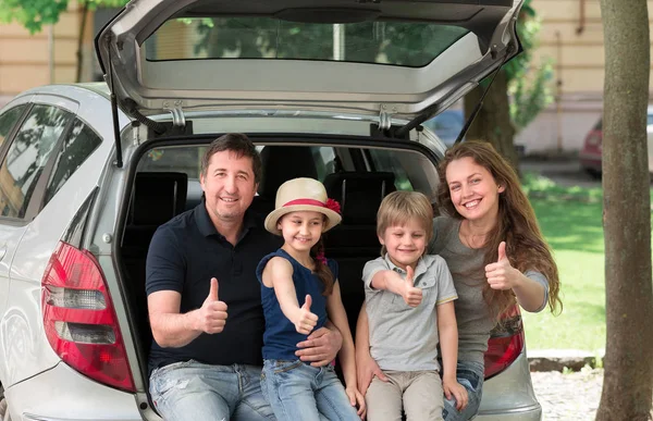 Šťastná rodina sedí v kufru auta a ukazuje palce — Stock fotografie