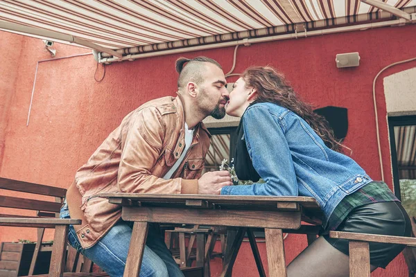 Молодая пара целуется сидя за столом в уличном кафе — стоковое фото