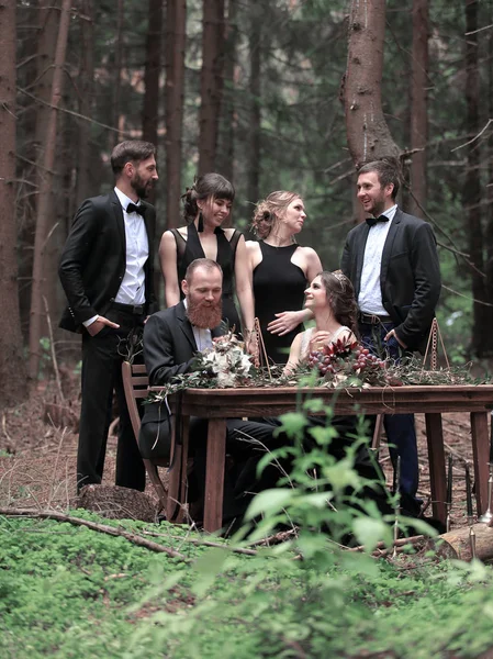 Ospiti e un paio di novelli sposi vicino al tavolo da picnic nel bosco — Foto Stock