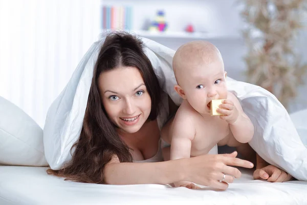 Happy mother plays with the baby lying on the bed — Stock Photo, Image