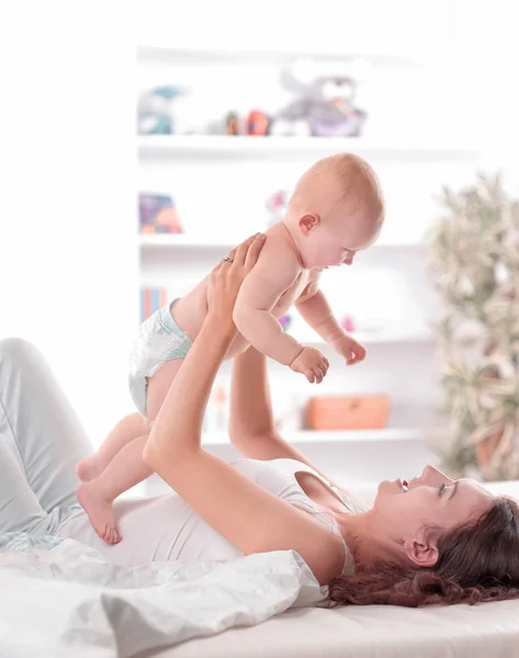 Jovem mãe brinca com o bebê deitado na cama — Fotografia de Stock