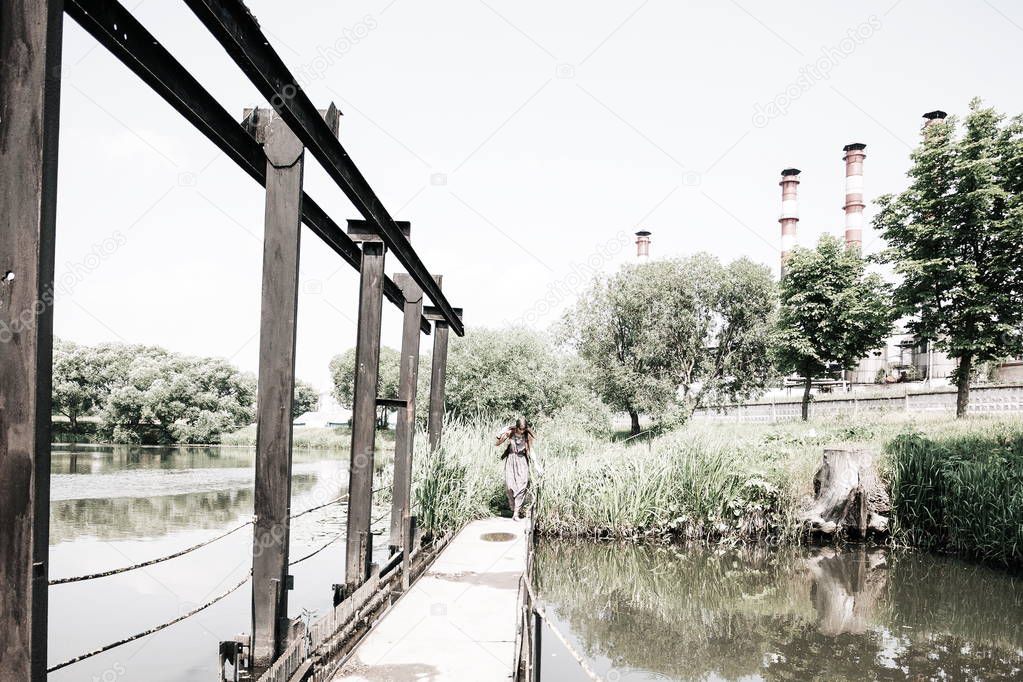 young hippie woman standing on wooden bridge on summer day
