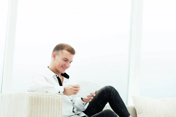 Homem sorridente com tablet digital sentado no sofá em sua sala de estar — Fotografia de Stock