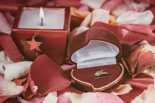 Kaars en een diamanten ring op een achtergrond van rozenblaadjes — Stockfoto
