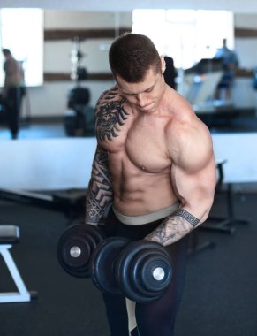 Kaslı adam pazı üzerinde dambıl ile egzersiz yapıyor