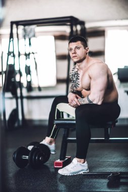 yorgun erkek vücut geliştirmeci spor salonunda bir bankta oturan.