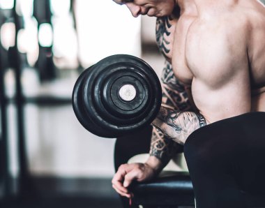 vücut geliştirmeci adam bir bankta oturur ve onun pazı için egzersizler gerçekleştirir.