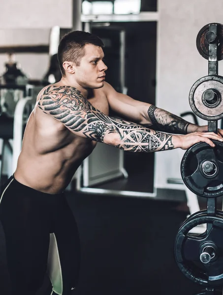 Αρσενικό bodybuilder με ένα τατουάζ στο χέρι του στέκεται στο γυμναστήριο — Φωτογραφία Αρχείου