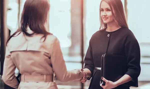 Two girls shaking hands in modern office, smiling and looking at — Stock Photo, Image