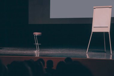 konferans salonunda podyumda boş ekran, mama sandalyesi ve flipchart