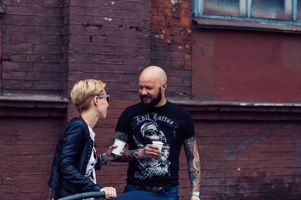 ベラルーシ、ミンスク、2015年5月17日、オクチャバースカヤ通り、バイカーフェスティバル。街の建物の近くでコーヒーを飲むバイカーのカップル. — ストック写真