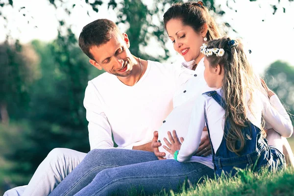 Pais expectantes e sua filhinha sentada na grama — Fotografia de Stock