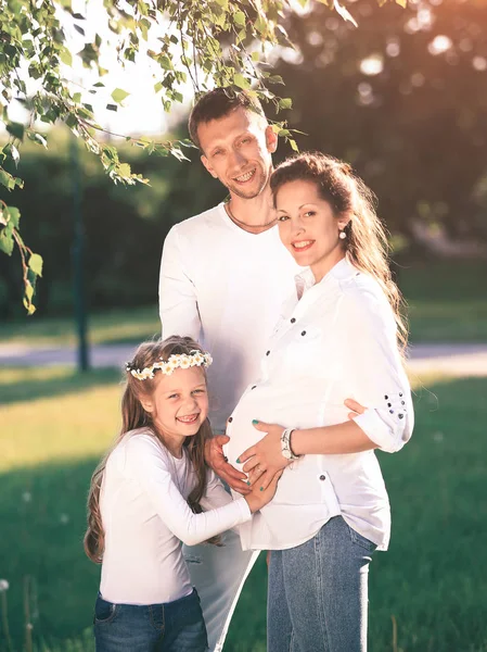 Glücklicher Vater und kleines Mädchen umarmen ihre schwangere Mutter auf einer wa — Stockfoto