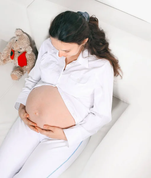 Nahaufnahme. Schöne schwangere Frau mit einem Stofftier auf der Couch liegend. — Stockfoto