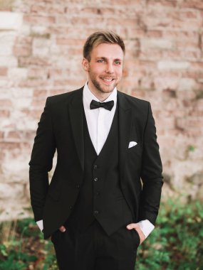 Gülümseyen damat eski tuğla duvarın arkasında.