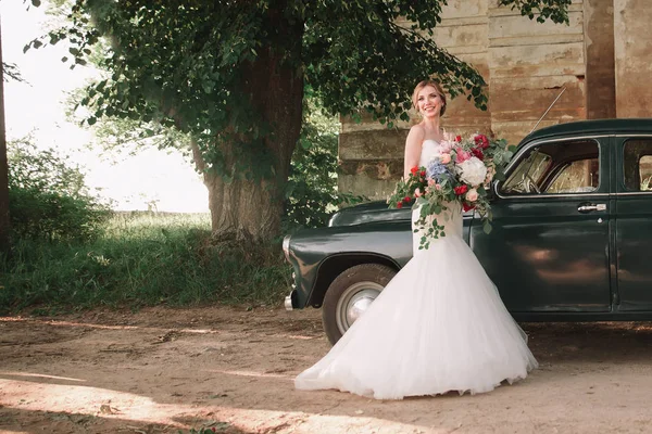 Felices recién casados de pie junto a un coche con estilo durante el paseo —  Fotos de Stock