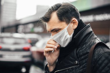 Sigara yakan koruyucu maskeli ciddi bir adam.