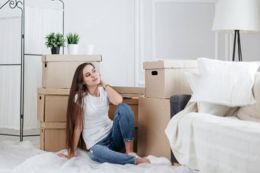 Mutlu genç bir kadın yeni dairesinde yerde oturuyor.