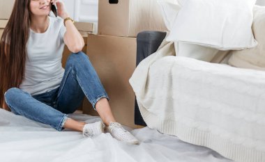 Genç bir kadın yeni bir dairede akıllı telefonundan sipariş veriyor.