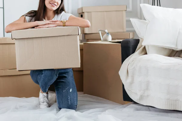 Mujer joven con una caja de cartón sentada en el suelo en un apartamento nuevo — Foto de Stock