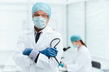 Kapat. Laboratuvarda duran koruyucu maskeli bir doktor..