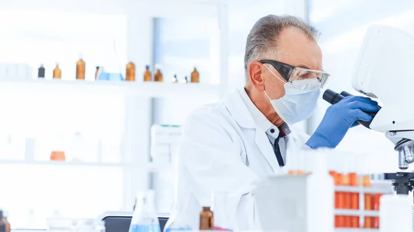 Cientista em uma máscara protetora realiza pesquisa no laboratório. — Fotografia de Stock