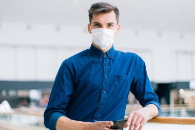 Sokakta duran akıllı telefonlu koruyucu maskeli bir adam.