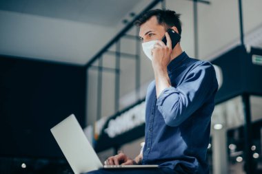 Koruyucu maskeli genç adam akıllı telefonundan bir bağlantı seçiyor.
